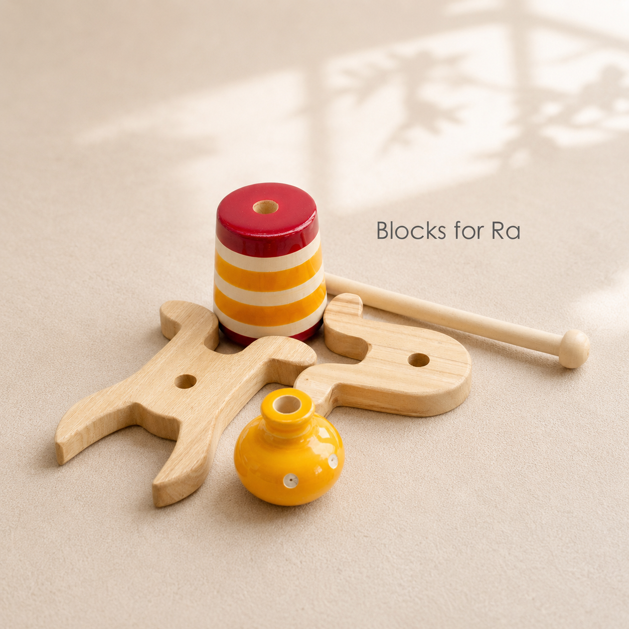 Set of wooden toys including a striped cylindrical block, a yellow ball, and a wooden figure on a beige surface.