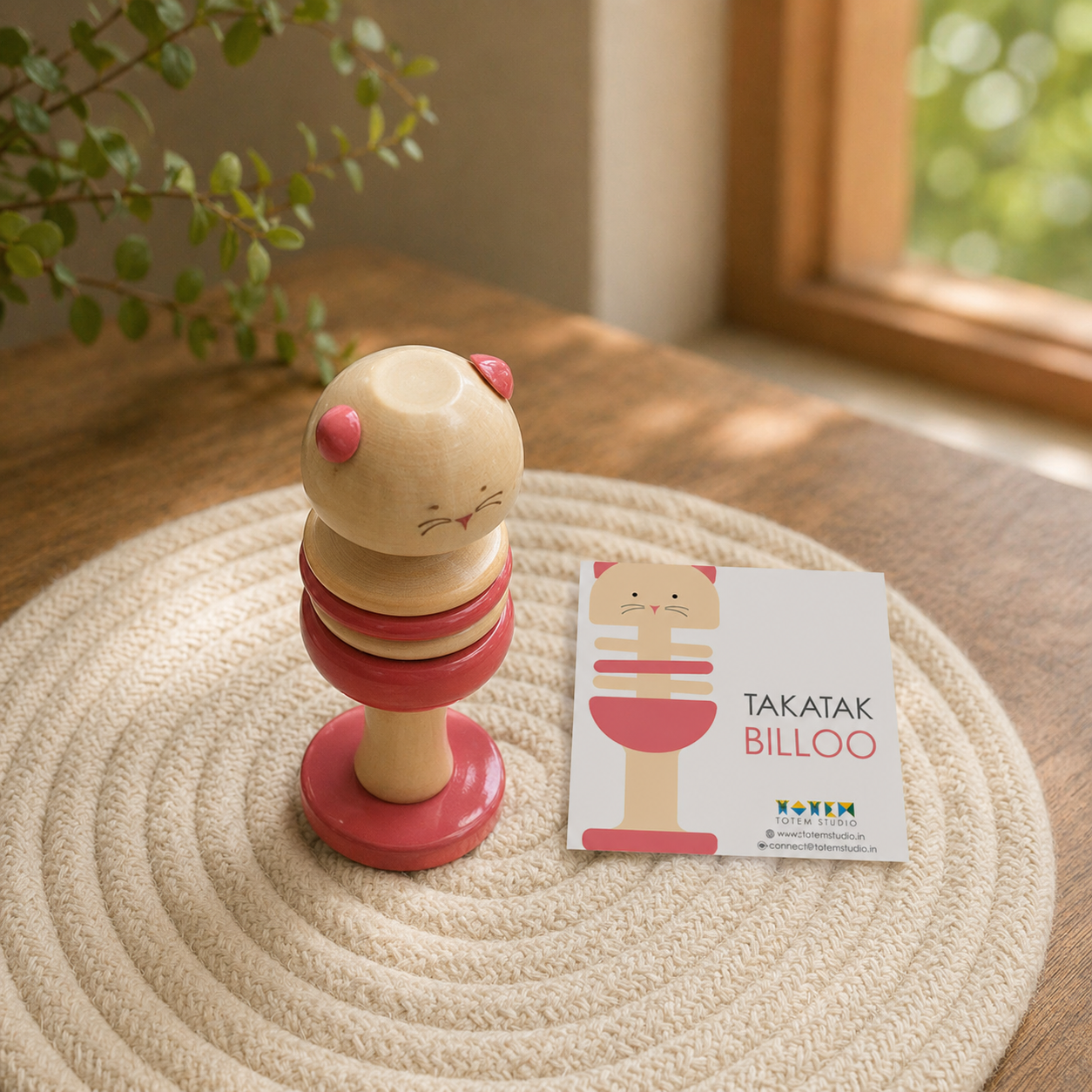 Wooden toy with pink accents on a textured surface next to a card, handcrafted in channapatna