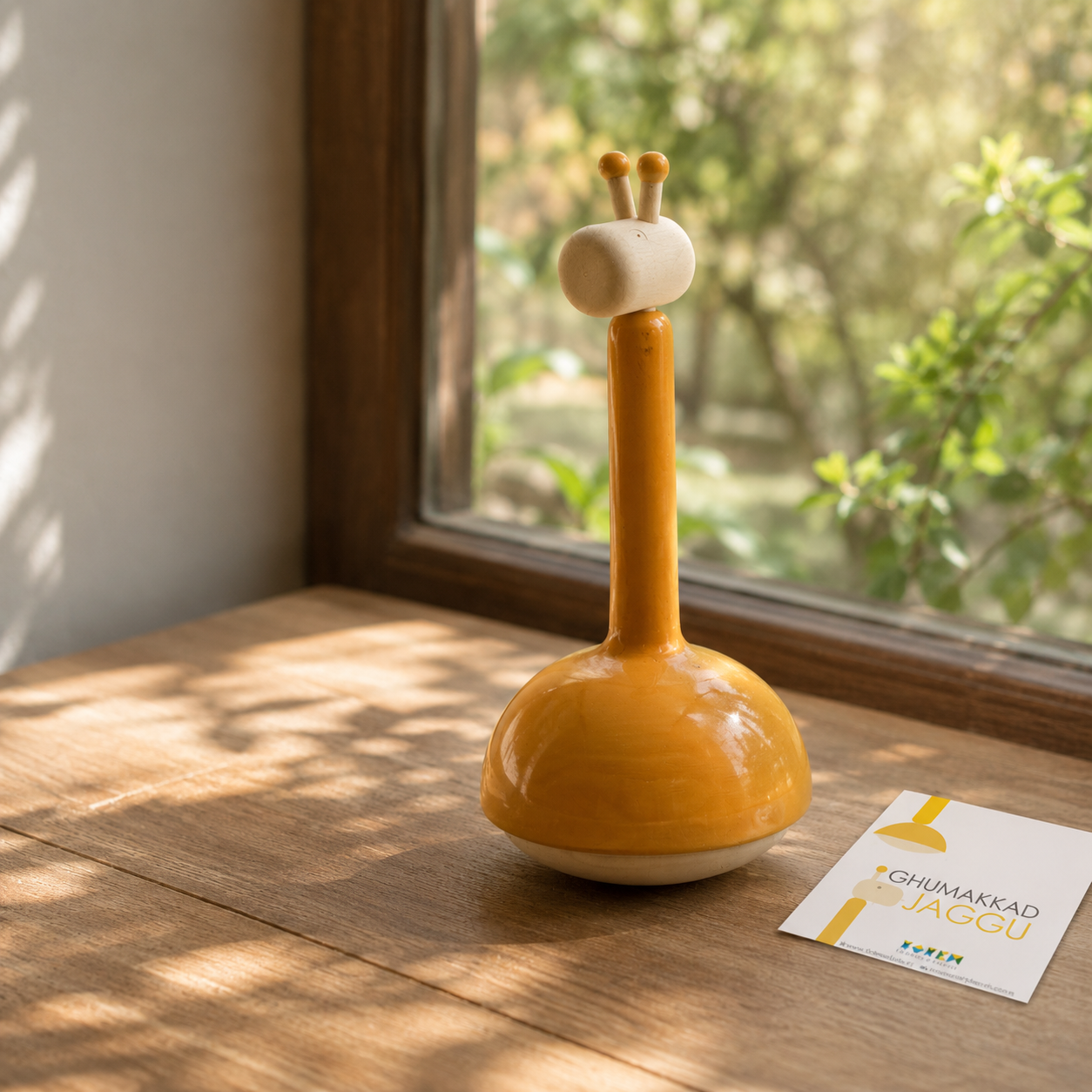 Yellow giraffe-shaped object on a wooden surface with a window in the background