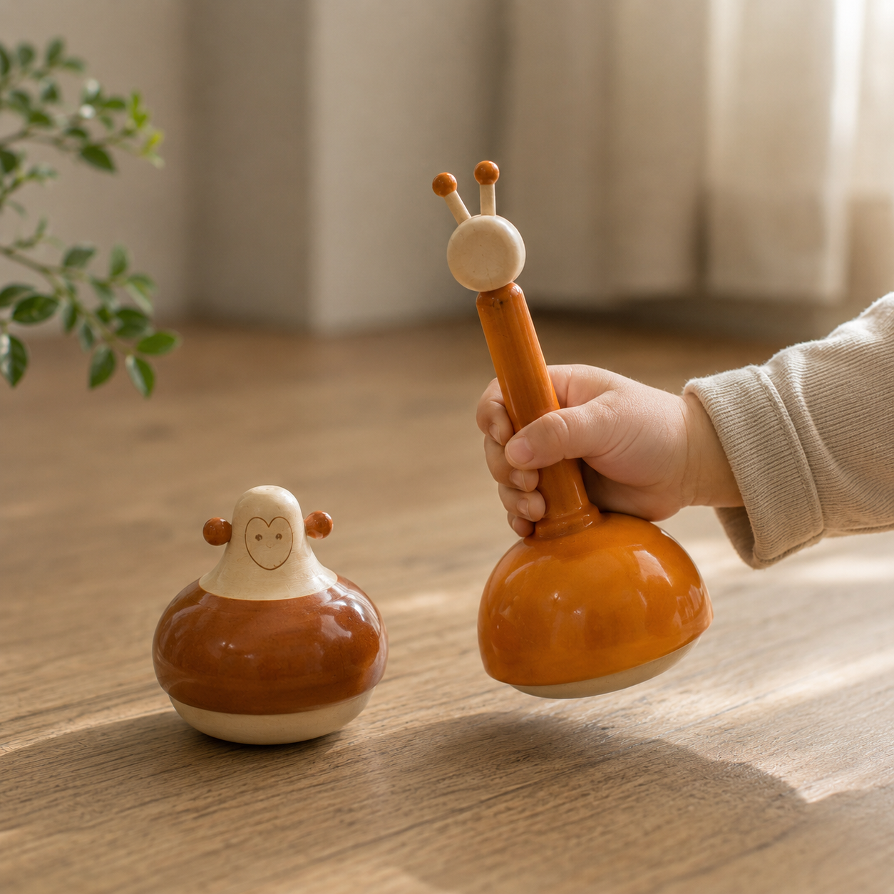 A child`s hand holding a giraffe rattle with monkey rattle roli-poli on the floor.